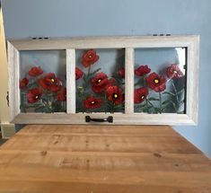 three pane window with red flowers in it on a wooden table next to a blue wall