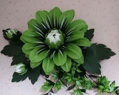 a large green flower sitting on top of a white table next to other flowers and leaves