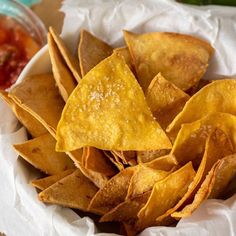 some tortilla chips in a white bowl with salsa and ketchup on the side