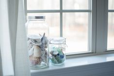 two glass jars with seashells sit on a window sill