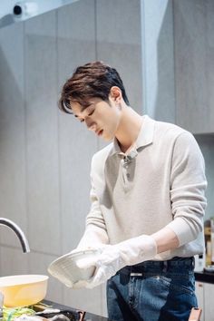 a young man wearing white gloves is washing dishes in the kitchen with his hands and looking down