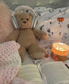 a brown teddy bear sitting on top of a bed next to an open book and candle