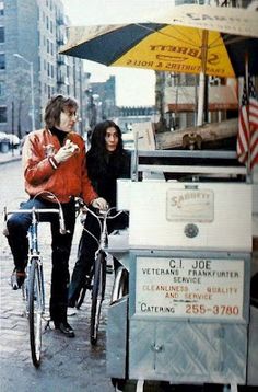 two people sitting at an ice cream cart on the side of the road with bicycles