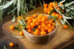 small orange berries in a wooden bowl on a cutting board with olives and leaves