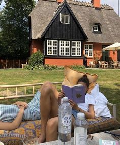 two people are sitting on a bench reading books and drinking water in front of a house