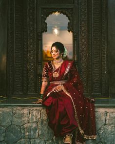 a woman sitting on top of a stone wall wearing a red dress and gold jewelry