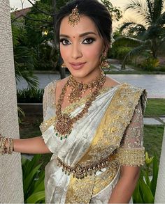 a woman in a white and gold sari posing for the camera with her hands on her hips