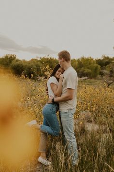 a couple cuddles in the tall grass during their engagement photo session at sunset