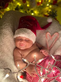 a baby wearing a santa hat is laying on a blanket with christmas lights around it