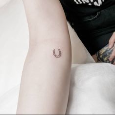 a small horseshoe tattoo on the left inner arm and lower arm, with a woman's leg behind her