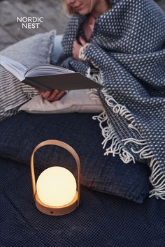 a woman reading a book while sitting on the floor next to a light that is turned on