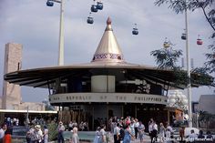 many people are walking around in front of a building that has a carousel on top