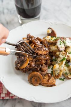 a person is holding a fork over some food on a plate with mushrooms and potatoes