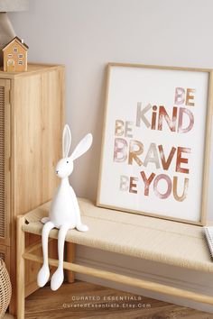 a white rabbit sitting on top of a wooden bench next to a framed letter print