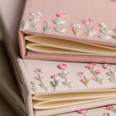 three pink notebooks with embroidered flowers on them