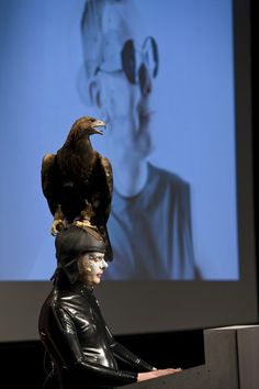 an eagle sitting on top of a man's head in front of a screen