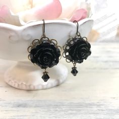 Lovely black rose earrings can be worn any time of year. These earrings are light weight and comfortable to wear. The French hook ear wires are lead free hypoallergenic. The roses are made of durable resin.  Measuring from the loop of the French wire down is 1 1/4" long  x 1" wide Your beautiful earrings come equipped with "French Wire Keepers" - little rubber stoppers to keep your earrings in place comfortably.   You will receive your earrings carefully packaged in a gift box and shipped with USPS Ground Advantage (formerly called First Class Mail) in a padded mailer with tracking. Jewelry Care: To keep your handmade jewelry looking lovely protect it from hair spray, perfume and other chemicals as it can affect the luster of your jewelry. Remove before bathing, swimming or sleeping. Clean Black Dangle Flower Earrings With Ear Wire, Black Flower Drop Earrings For Gift, Adjustable Black Flower Earrings For Pierced Ears, Adjustable Black Flower Earrings, Handmade Adjustable Black Flower Earrings, Black Rose Design Party Jewelry, Black Bohemian Dangle Flower Earrings, Bohemian Black Dangle Flower Earrings, Bohemian Black Flower Earrings For Gift