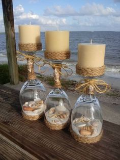 three candles sitting on top of a wooden table next to the ocean in glass bottles