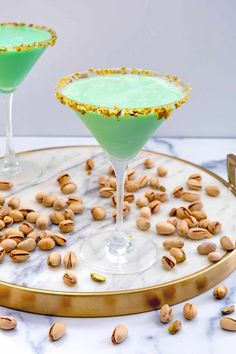 two glasses filled with green liquid and nuts on a marble tray next to each other