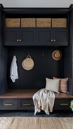 a black bench with some baskets on it and two coats hanging from the back wall