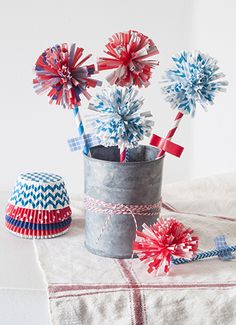 red, white and blue paper flowers in a bucket on a table with a hat