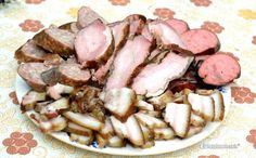 a plate full of sliced meat and potatoes on a tablecloth with flowers in the background