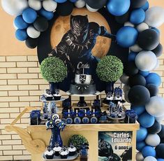 a table topped with blue and white balloons next to a batman themed dessert bar filled with cupcakes