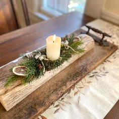 a candle is lit on top of a wooden tray with greenery and pine cones