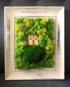 a white frame with moss and a small house in the center is surrounded by green plants