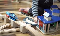 a child playing with wooden train set on the floor in a play area at a children's museum