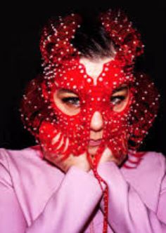 a woman wearing a red mask covering her face and hands with beads around her eyes