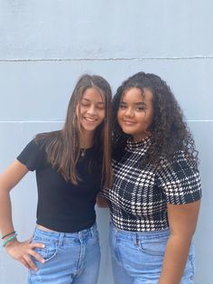 two young women standing next to each other in front of a blue wall with their hands on their hips