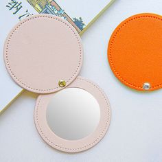 two round mirrors sitting next to each other on top of a white table with an orange circle