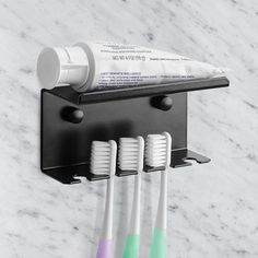 three toothbrushes are hanging on the wall next to a toothpaste holder