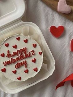 a white cake with red frosting and hearts on it sitting in a plastic container