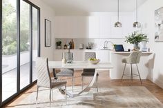 a kitchen with white walls and wooden flooring next to a dining room table surrounded by chairs