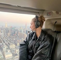 a woman wearing headphones sitting in an airplane looking out the window at the city