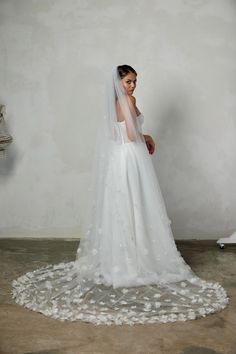 a woman in a wedding dress with a veil over her head and flowers on the floor