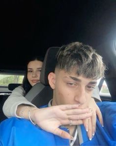 two people sitting in the back seat of a car, one is covering his mouth