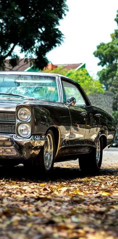 an old car is parked on the side of the road in front of some trees