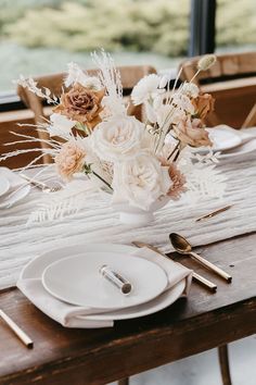 the table is set with white plates and silverware, flowers in a vase on top