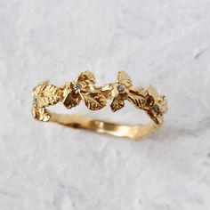 a gold ring with leaves and diamonds on it, sitting on a white stone surface