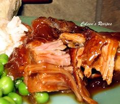 a green plate topped with meat and rice covered in gravy next to peas