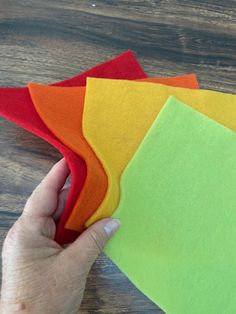 someone is holding four different colored felts on a table with one hand and the other