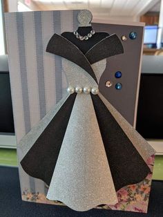 a card with a black and silver dress on it's front, decorated with pearls