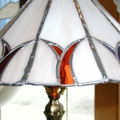 a stained glass lamp with chain hanging from it's base, in front of a window