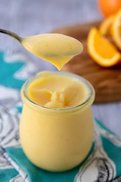 a spoon full of orange custard on top of a jar with an orange in the background