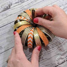 a woman is holding some ribbon on top of an orange and white striped pumpkin ornament