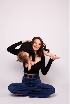 a woman sitting on the floor holding a baby up to her head and smiling at the camera