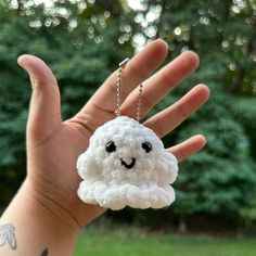 a hand holding a small white cloud keychain with a smiley face on it